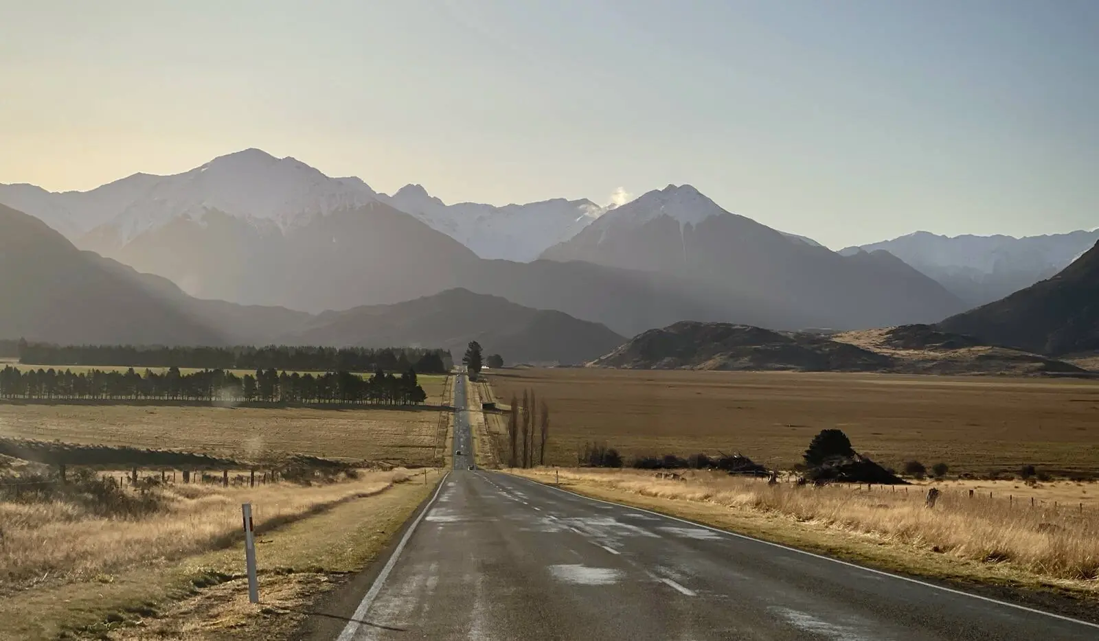 An empty road crossing open tussock country towards distant mountains